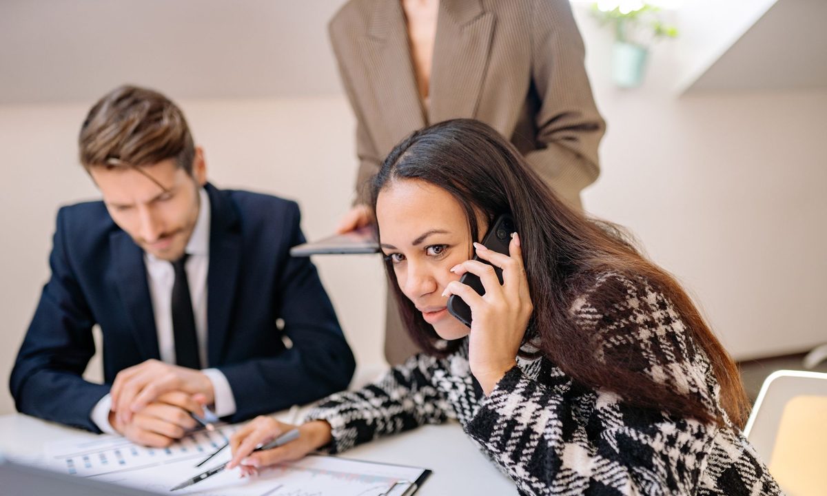 A busy office — one person taking a call while colleagues work through paperwork at the same desk.